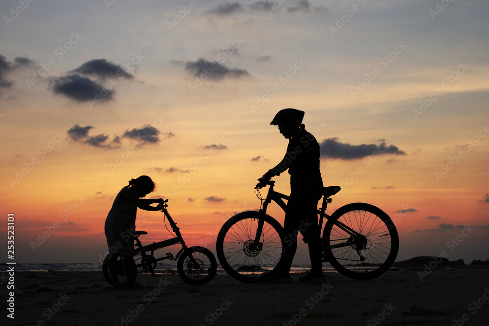 Fototapeta premium Silhouette of stepmother alone with children and bicycle at sunset background