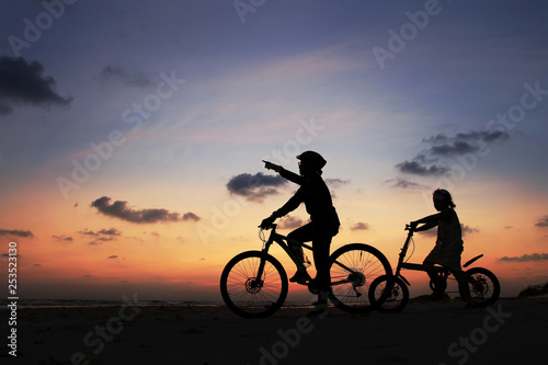 Silhouette of stepmother alone with children and bicycle at sunset