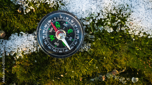 compass with the arrow directed to the north which lies on the frozen and snow-covered wood moss in the cold northern forest