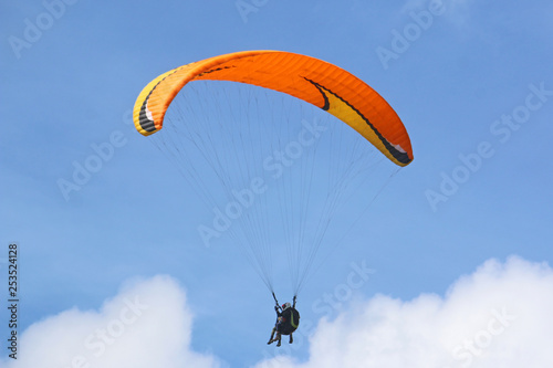 Tandem paraglider flying orange wing