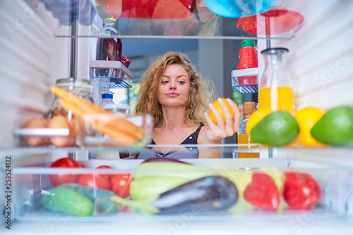 Woman taking orange for breakfast from fridge. Picture taken from the inside of fridge.