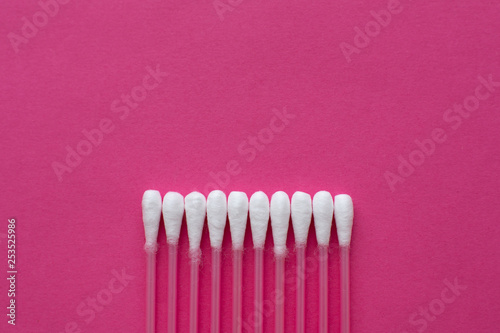 Closeup top view on cotton buds laid in a horizontal line on pink background