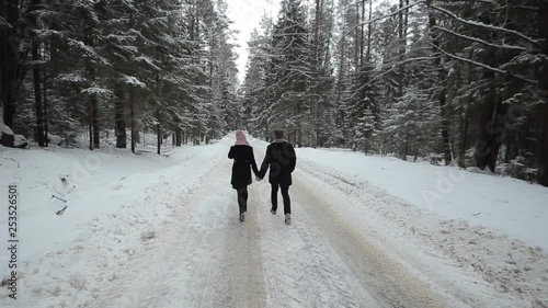 Back view of young and beautiful couple is walking in the winter forest. Milennials man and woman having fun. Winter season. photo