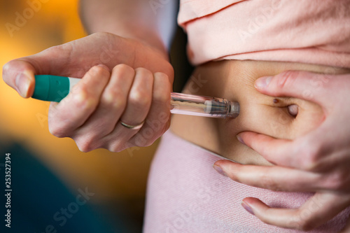 Woman making hormonal therapy injection into her belly. Close up syringe pen. Person in bedroom  in vitro fertilisation treatment.