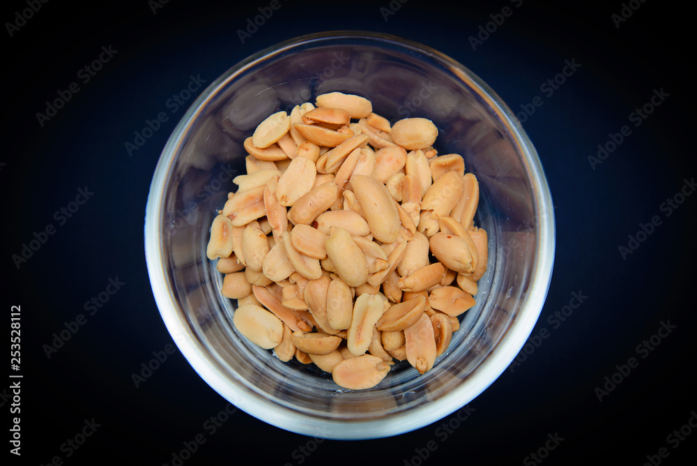 Peeled and salted peanuts in a glass bowl. Isolated on a dark blue background Peeled and salted peanuts in a glass bowl. Isolated on a dark blue background
