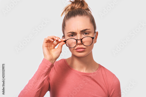 Close up portrait of young woman frowning puzzled teacher looking serious. Beautiful female woman in eyewear looking at camera. People emotions
