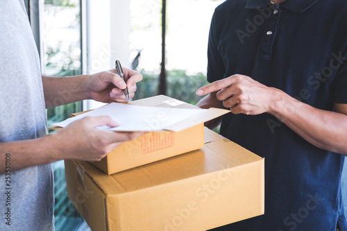 Delivery mail man giving parcel box to recipient, Young man signing receipt of delivery package from post shipment courier at home
