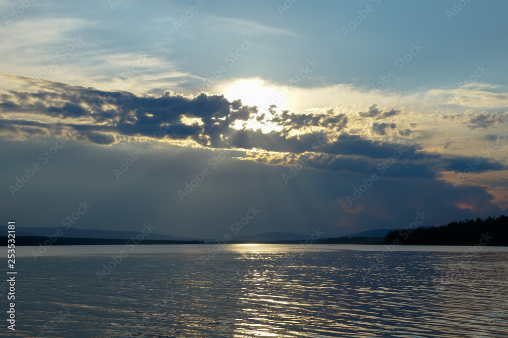The setting sun looks out from the oncoming thundercloud. Twilight landscape on the reservoir