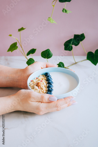 Healthy breakfast bowl with muesli and yogurt in woman hands on pink and marble background. Clean eating, vegetarian, vegan, alkiline diet food concept photo