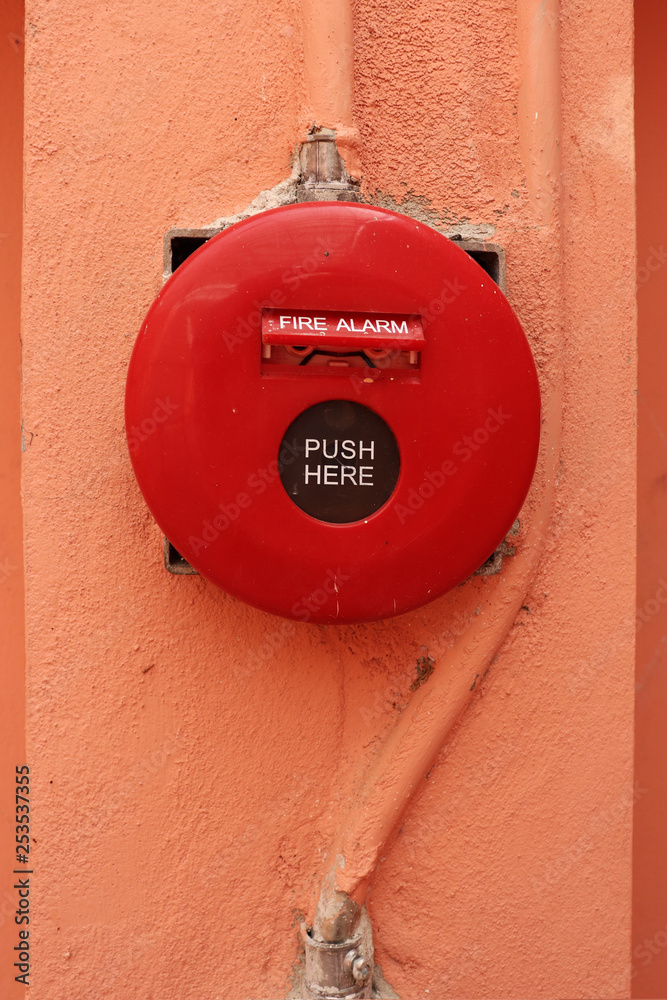Red fire alarm on orange wall.