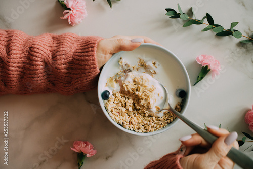 Woman in coral woolen sweater eating breakfast bowl with muesli and yogurt, berries and hazelnuts. Clean eating, vegetarian, vegan, alkiline diet food concept photo