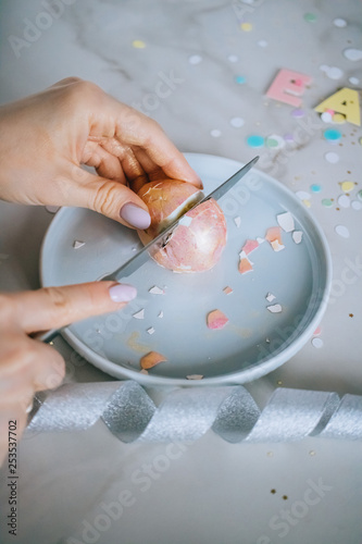 Girl cutting golden easter eggs on marble background, confetti, sparkles, ribbons.