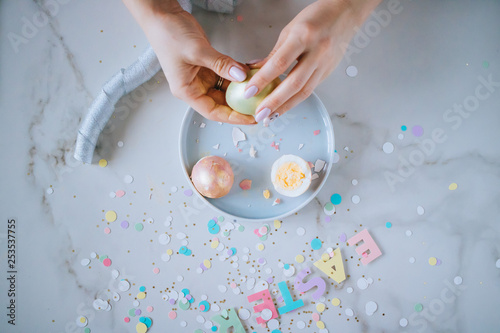 Girl breaks golden easter eggs on marble background, confetti, sparkles, ribbons.