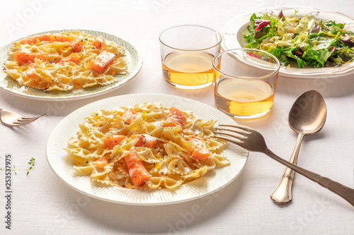 Pasta and wine, Italian dinner. Farfalle with smoked salmon and cream sauce, served with mesclun salad leaves