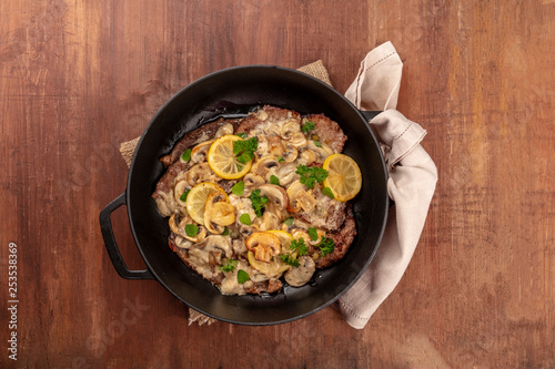 Scallopine di vitello, veal scallopini, a traditional Italian dish with mushrooms, lemons, and parsley, shot from above in a pan with copy space
