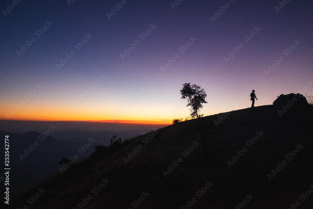 Silhouette of a man reaching the top of the hill in a sunset background in Thailand.