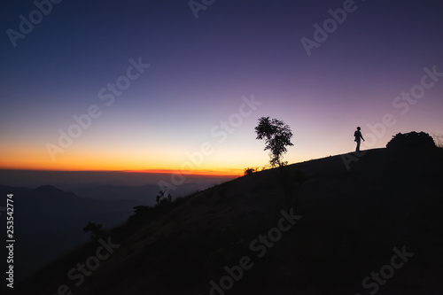 Silhouette of a man reaching the top of the hill in a sunset background in Thailand.