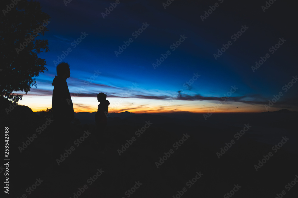 Two silhouette of people watching the sunrise on top of a mountain in northern part of Thailand.