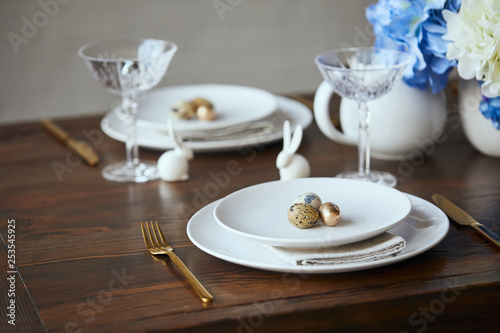 Selective focus of quail eggs on white plates, crystal glasses and decorative bunnies on wooden table at home