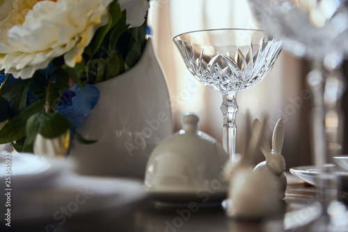 selective focus of crystal glass near flowers in vase and decorative rabbits on wooden table at home photo