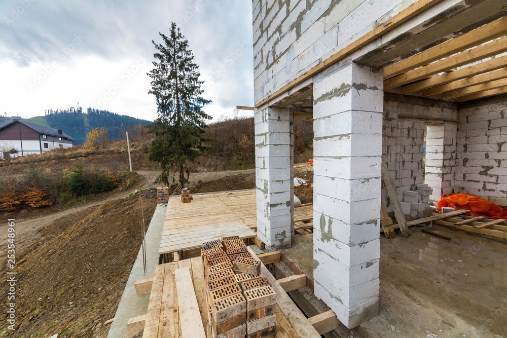 House building under construction basement detail with walls made of large hollow foam insulation blocks, wooden logs frame for first floor ceiling and brick supporting columns in rural area. House building under construction basement detail with walls made of large hollow foam insulation blocks, wooden logs frame for first floor ceiling and brick supporting columns in rural area.