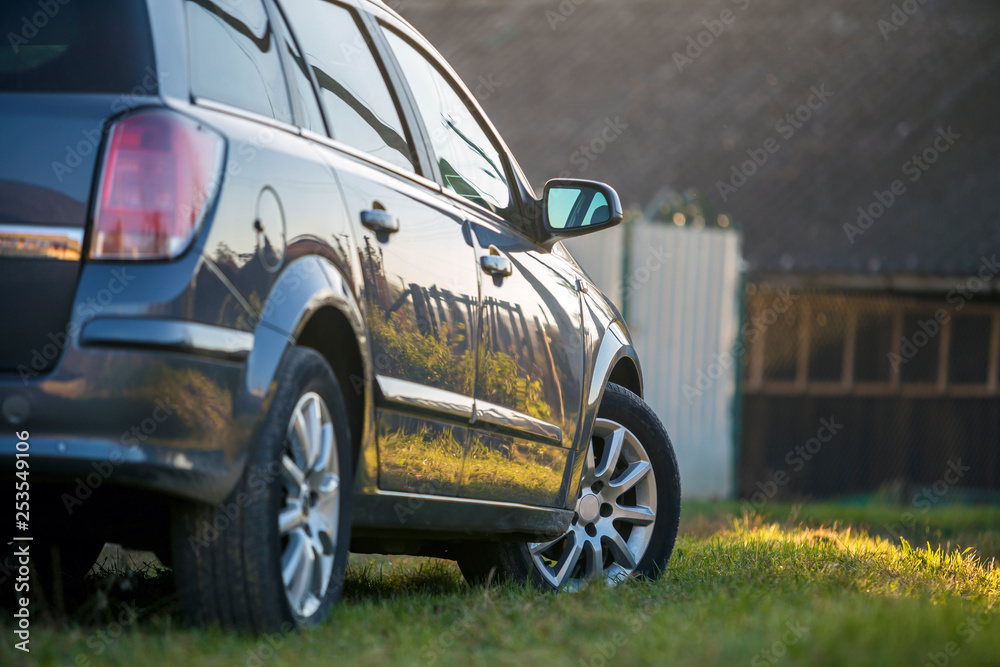 New shiny gray car parked on green grass on blurred sunny summer rural background.