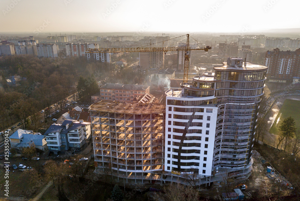 Apartment or office tall building under construction, top view. Tower crane and city landscape stretching to horizon. Drone aerial photography.
