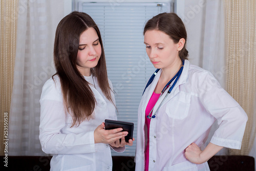 Two female doctors or nurses look at the tablet and discuss therapy