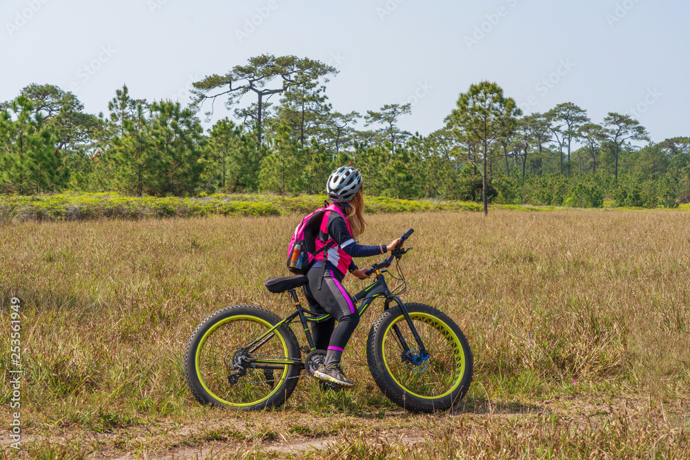Female cyclist standing on mountain bike with grass field background Female cyclist standing on mountain bike with grass field background