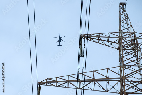 Concept helicopter flies against the blue sky and electric wires. Modern world. Iron bird and electricity. Minimalism in colors. Geometry in the image