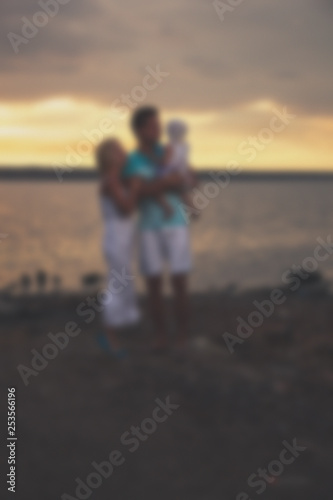 Blurred young family father mother and daughter at sunset on the lake.