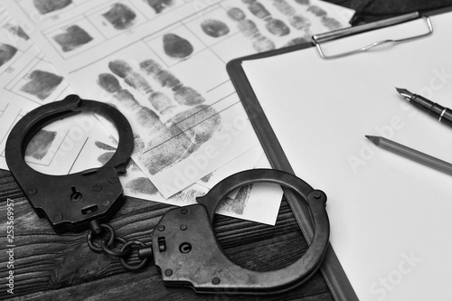 Handcuffs, fingerprints of the detained criminal, a blank sheet of paper on the background of a wooden table. photo