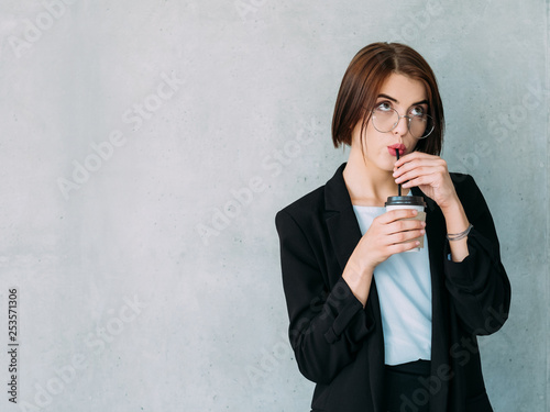 Corporate worker at break. Curious young woman sipping coffee and looking up. Copy space on grey background. photo