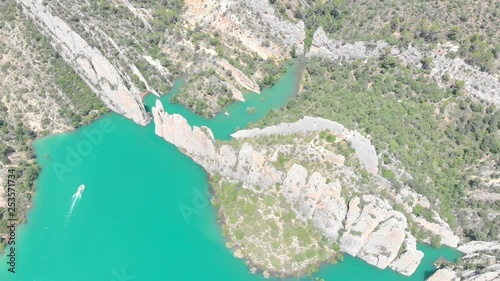 Aerial view of a rock wall formation with a turquoise lake. Natural look alike Chinese wall with a castle on top of the fortification. A boat is riding on the lake. Muralla de Finestres. photo