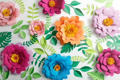 Fototapeta Naklejka Na Ścianę i Meble -  top view of colorful paper flowers and green leaves on grey background