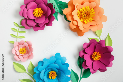 Fototapeta Naklejka Na Ścianę i Meble -  top view of multicolored paper flowers and green leaves on grey background