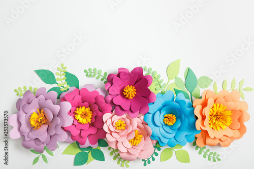 top view of multicolored paper flowers and green leaves on grey background