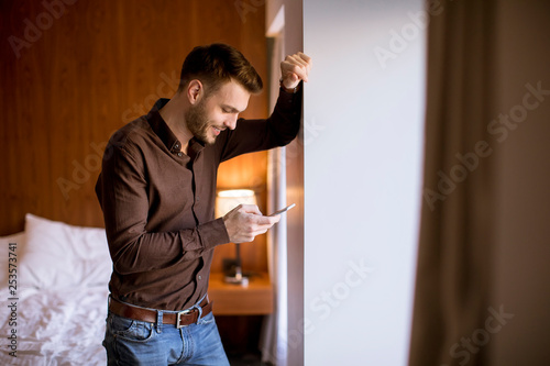 Young man using mobile phone in the room by window