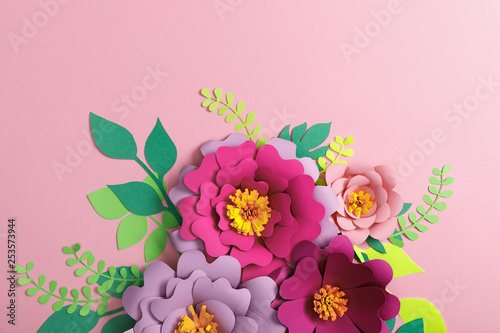 Fototapeta Naklejka Na Ścianę i Meble -  top view of multicolored paper flowers and green leaves on pink background