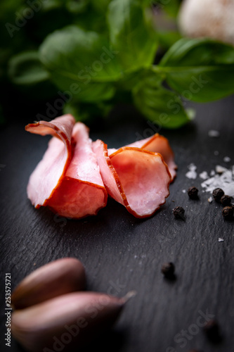 Plasterki swojskiej wędliny. Wędzona kiełbasa w papierze na kuchennym ciemnym blacie.