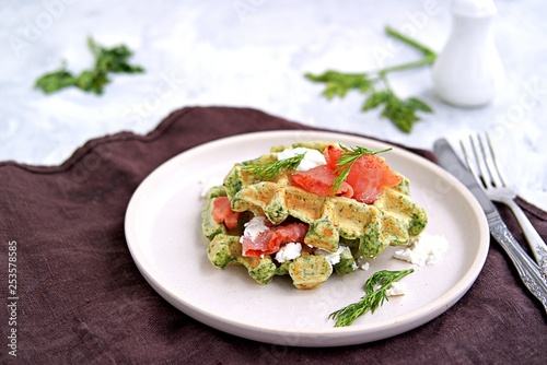 Light dinner, lunch or brunch, savory spinach snack waffles with salted salmon and cream cheese on a ceramic plate.