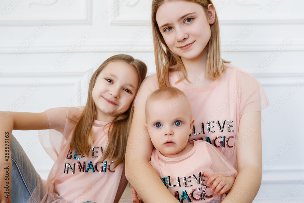 Light family series. Three sisters on a white background, dressed in funny  t-shirts and jeans Stock Photo | Adobe Stock