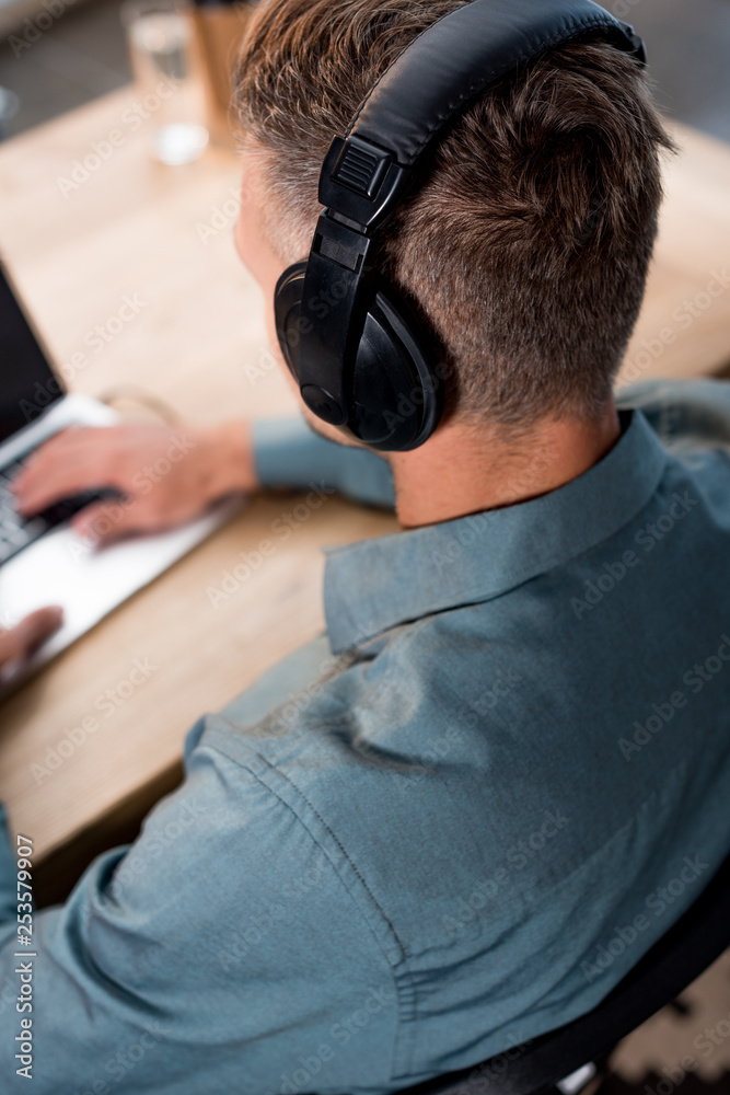 overhead view of businessman listening music in headphones while using laptop