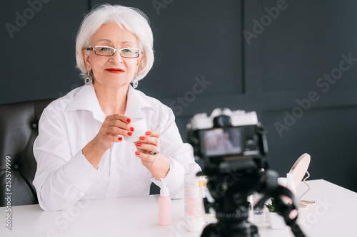 Successful senior woman. Blogging business lifestyle. Elderly lady making video presenting skin care product. Copy space. photo