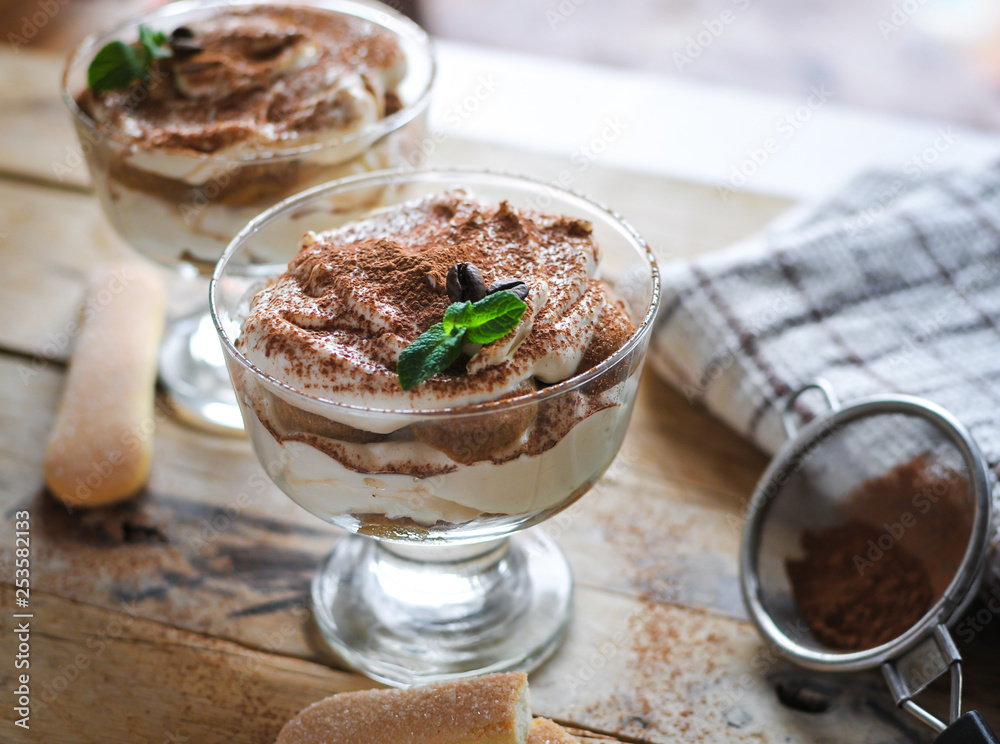 Close-up of classic tiramisu cake in a glass with fresh mint, on wooden background Close-up of classic tiramisu cake in a glass with fresh mint, on wooden background