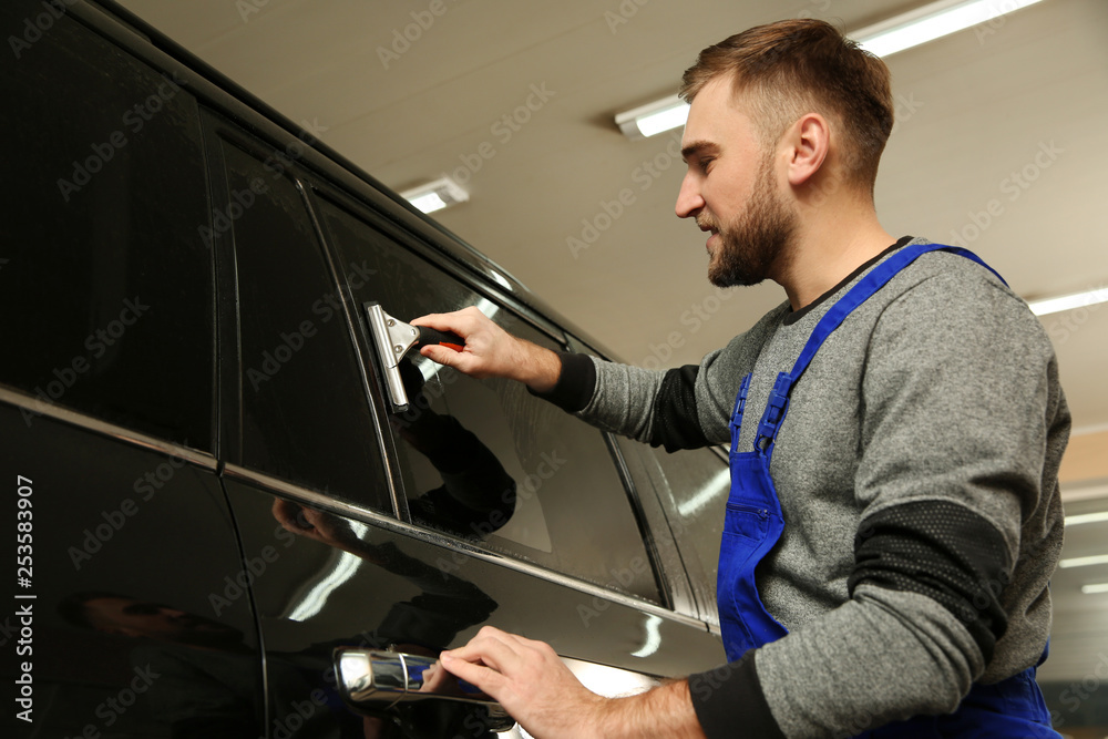 Skilled worker washing tinted car window in shop Skilled worker washing tinted car window in shop