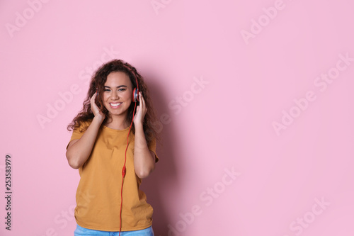 African-American girl listening to music with headphones on color background, space for text