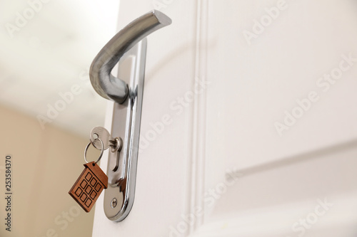 Key with house-shaped trinket in door lock, closeup. Space for text