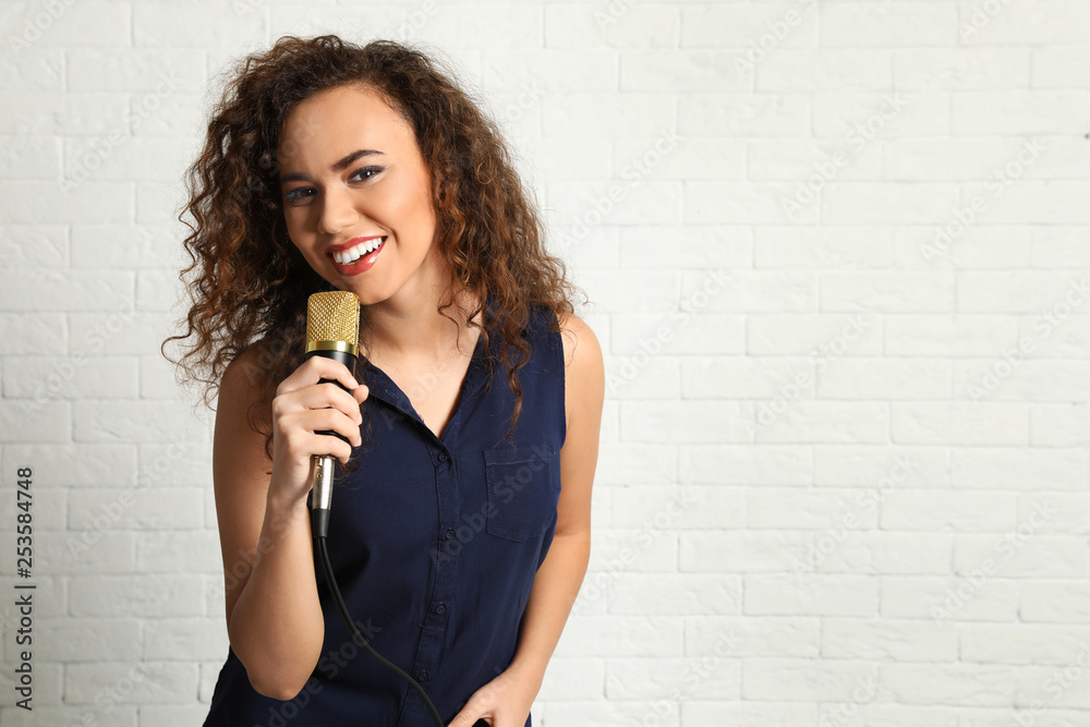 Portrait of curly African-American woman in blouse posing with microphone near brick wall. Space for text Portrait of curly African-American woman in blouse posing with microphone near brick wall. Space for text