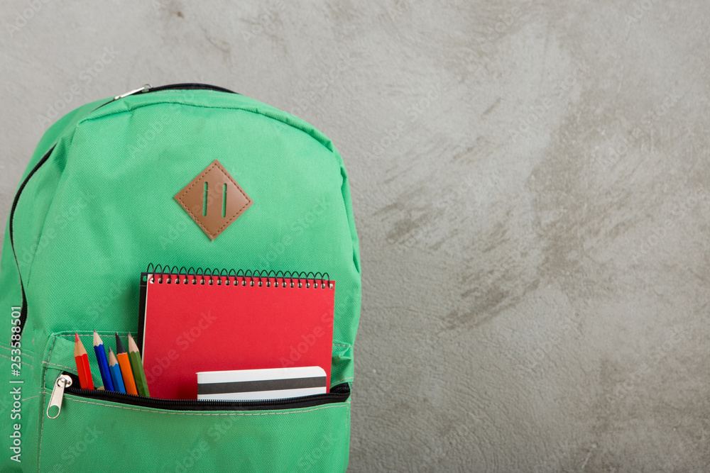 Naklejka premium green backpack, red notebooks and pencils against a cement wall